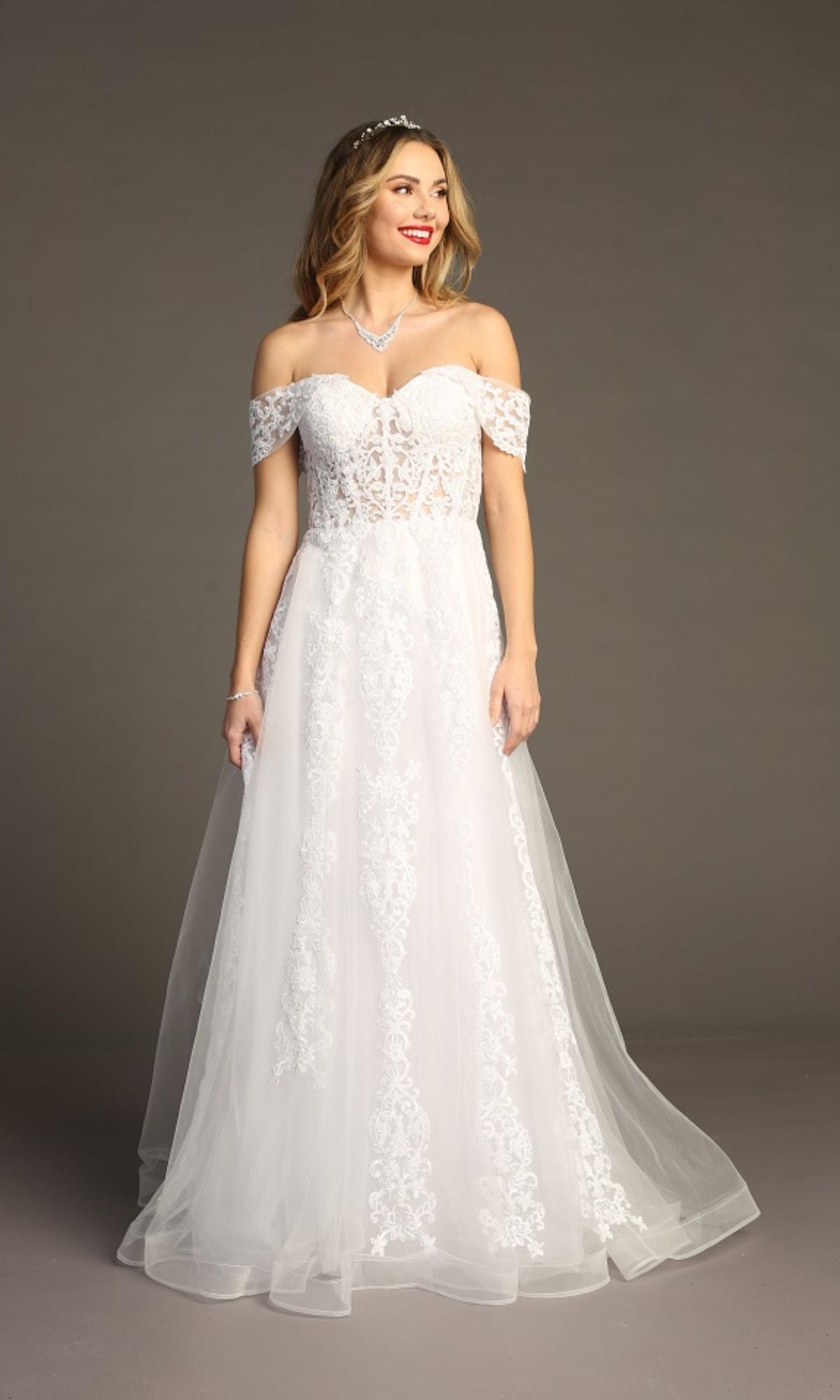 A woman wears the Long Lace Prom Ball Gown: Chicas CA1103, featuring an off-the-shoulder lace design with a sheer bodice and A-line skirt, standing against a plain studio background.